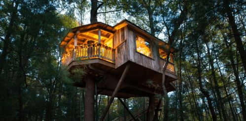 A cozy wooden treehouse illuminated at dusk, nestled among tall trees in a serene forest setting.