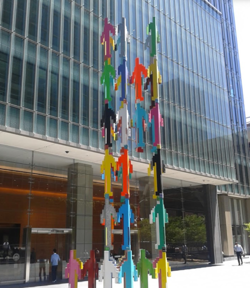 Colorful abstract sculpture of human figures in front of a modern glass building.