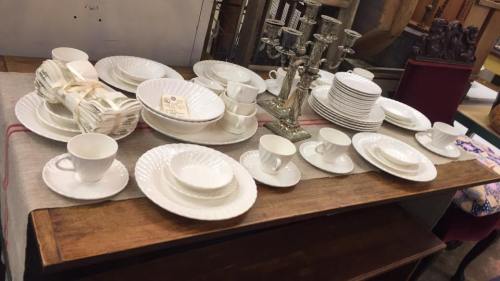 A wooden table displaying an assortment of white dishware, including plates, cups, and a silver candelabra.