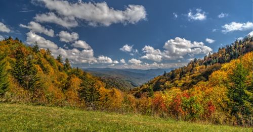 A scenic view of mountains with vibrant autumn foliage under a blue sky with fluffy clouds.