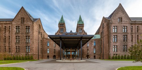 Historic brick building with twin spires, featuring a modern canopy and playground in the foreground.