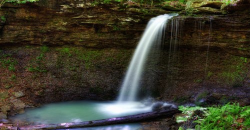 A serene waterfall cascades into a tranquil pool, surrounded by lush greenery and rocky cliffs.