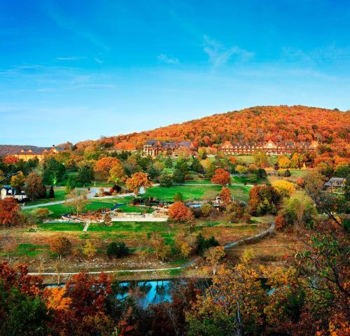 A scenic view of a colorful autumn landscape with rolling hills, trees, and a clear blue sky.