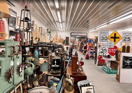 A bustling antique shop filled with various vintage items, holiday decorations, and signage along a spacious aisle.
