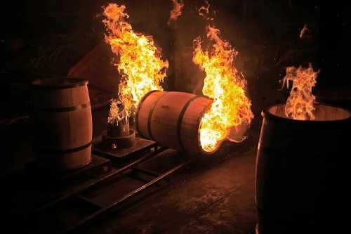 A wooden barrel on fire, surrounded by flames, with another barrel nearby in a dark setting.