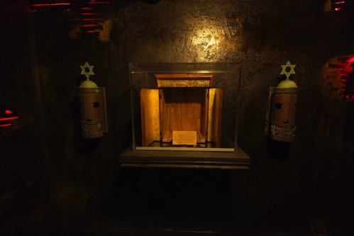 A dimly lit display case with a wooden interior and a plaque, flanked by two cylindrical objects with star motifs.