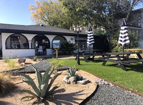 A cozy outdoor area with picnic tables, decorative plants, and striped umbrellas outside a charming building.