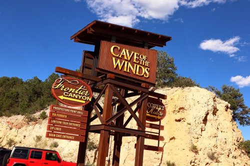 Sign for Cave of the Winds with attractions listed, set against a blue sky and rocky landscape.