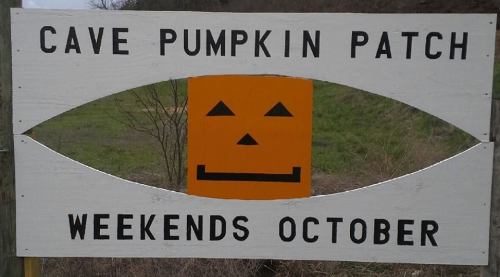 Sign for a pumpkin patch featuring a smiling jack-o'-lantern, stating "Cave Pumpkin Patch, Weekends October."
