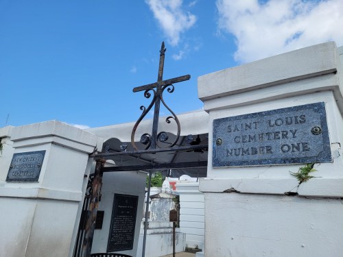 Entrance to Saint Louis Cemetery Number One, featuring a decorative cross and stone walls against a blue sky.