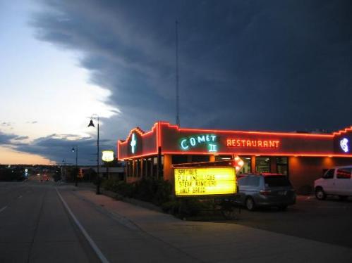 A neon-lit restaurant at dusk, with a dramatic sky and a sign advertising specials.
