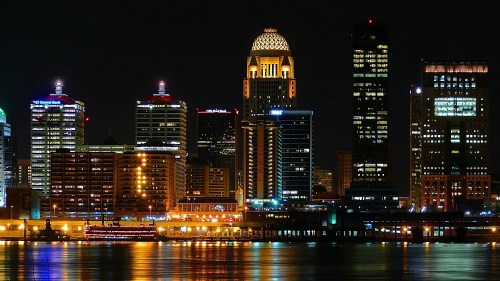 City skyline at night with illuminated buildings reflecting on the water.