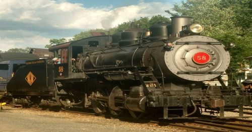 A vintage steam locomotive numbered 58, parked on tracks with a blue sky and trees in the background.