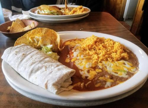 A plate of Mexican food featuring a burrito, taco, refried beans, and rice topped with cheese and lettuce.