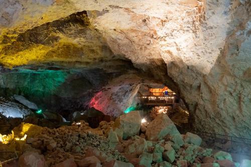A colorful cave interior with illuminated rock formations and a pathway leading to a wooden structure in the background.