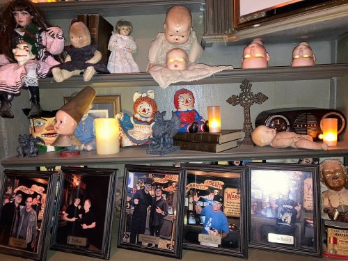 A shelf filled with vintage dolls, eerie figurines, and framed photos, illuminated by soft candlelight.