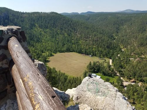 A panoramic view from a rocky outcrop overlooking a green valley and a cleared field surrounded by trees.