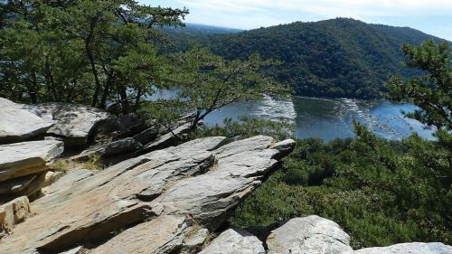 Scenic view of a river winding through green hills, framed by rocky outcrops and trees under a clear blue sky.