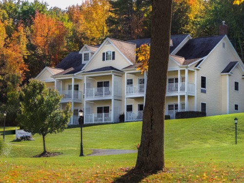 A yellow house with balconies surrounded by colorful autumn trees and a green lawn.