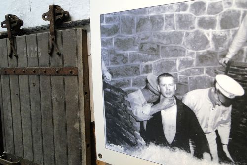 Black and white historical photo of a man being restrained, displayed next to a wooden door with metal hardware.