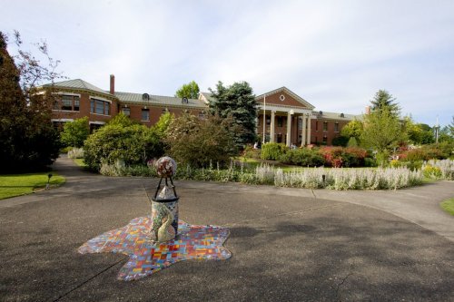 A brick building with columns surrounded by gardens and a colorful mosaic sculpture in the foreground.