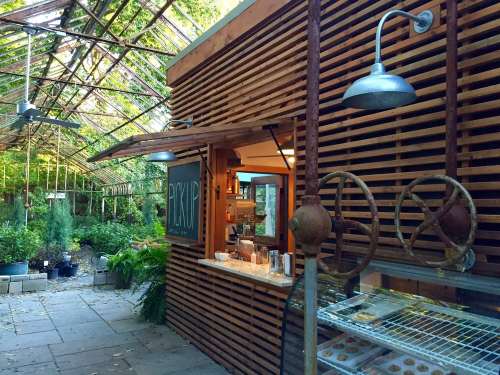 A rustic greenhouse with wooden walls, a service counter, and plants in pots, illuminated by overhead lights.
