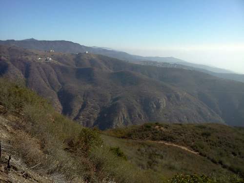 A panoramic view of rolling mountains and valleys under a clear blue sky, with sparse vegetation in the foreground.