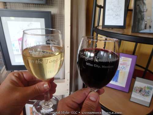 Two hands holding wine glasses, one with white wine and the other with red, in an art-filled setting.