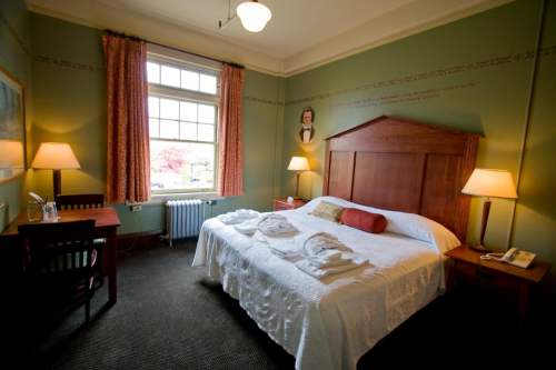 Cozy hotel room with a queen bed, desk, and warm lighting, featuring green walls and large windows.