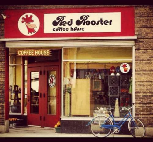 A cozy coffee house named "Red Rooster" with a red sign, large windows, and a blue bicycle parked outside.