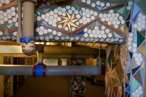 Colorful mosaic wall with hexagonal patterns and a decorative pipe featuring a whimsical face.