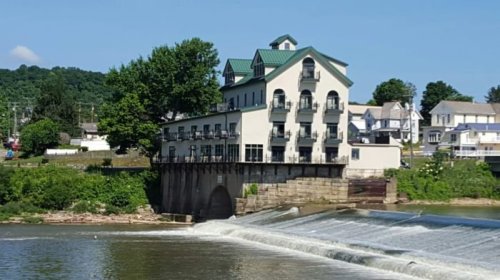 A riverside building with a green roof, overlooking a waterfall and lush greenery in the background.