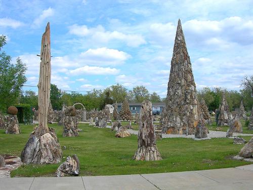 A unique outdoor sculpture park featuring tall stone and wood structures amidst green grass and a blue sky.