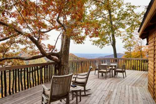 A wooden deck with chairs overlooks a colorful autumn landscape of mountains and trees.