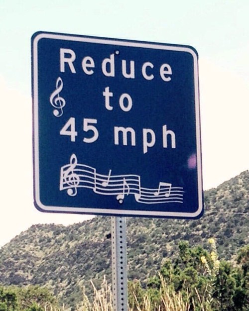 A road sign instructing drivers to reduce speed to 45 mph, decorated with musical notes.