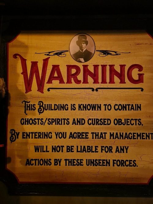 A sign warning of ghosts and cursed objects, stating management isn't liable for actions by unseen forces.