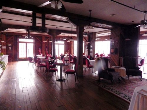 A spacious restaurant interior with wooden floors, red chairs, and large windows, creating a warm, inviting atmosphere.