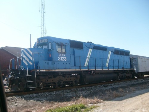 A blue freight locomotive with the number CEFX 3123 parked on a railway track under a clear sky.