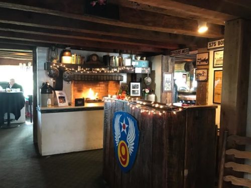 Cozy restaurant interior with a wooden bar, warm fireplace, and vintage decor, creating a welcoming atmosphere.