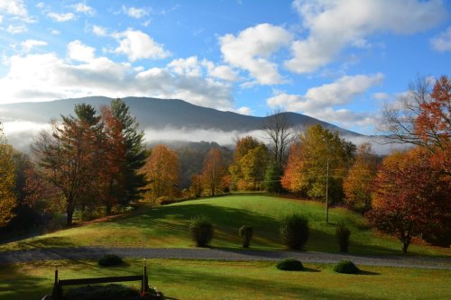 A scenic view of rolling hills and colorful autumn trees under a blue sky with fluffy clouds.