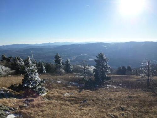 A scenic mountain view with snow-dusted trees and a clear blue sky, overlooking distant hills and valleys.