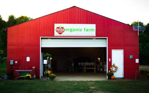 Red barn with "Wis Acres Organic Farm" sign, open garage door, and seasonal decorations outside.