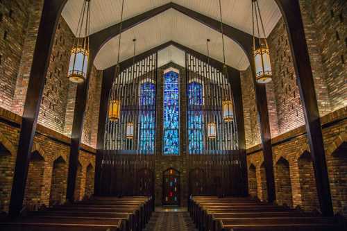 Interior of a church featuring wooden beams, stained glass windows, and rows of pews under warm lighting.