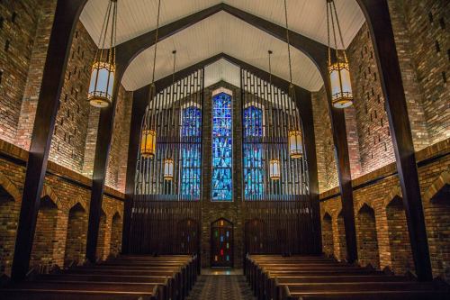 Interior of a church featuring wooden beams, stained glass windows, and rows of pews under warm lighting.
