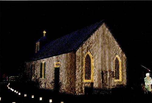 A charming church illuminated with festive lights against a dark night sky, creating a warm, inviting atmosphere.