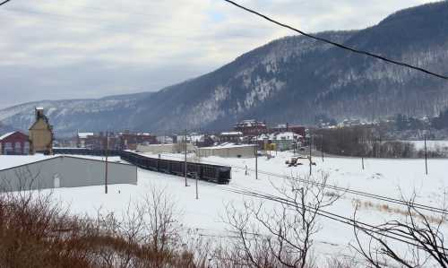 A snowy landscape with a train on tracks, mountains in the background, and a small town visible in the distance.