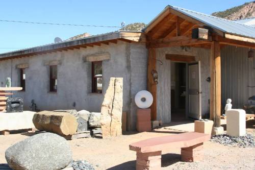 A rustic building with a wooden porch, stone sculptures, and a gravel path in a desert landscape.
