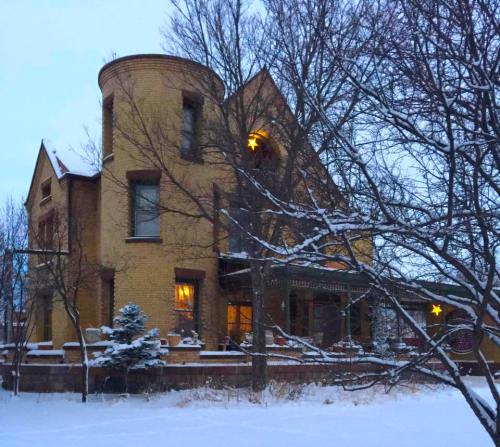 A snow-covered house with a round turret, surrounded by trees, featuring warm lights and a star decoration.