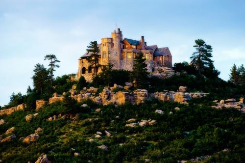 A stone castle perched on a rocky hill, surrounded by trees and bathed in warm sunlight.