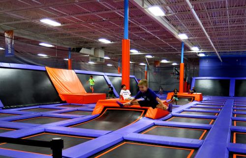 A vibrant indoor trampoline park with people jumping and playing on various trampolines and foam pits.